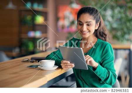 Pretty middle-eastern woman having lunch break at cafe, using pad Pretty middle-eastern woman having lunch break at cafe, using pad 82946381