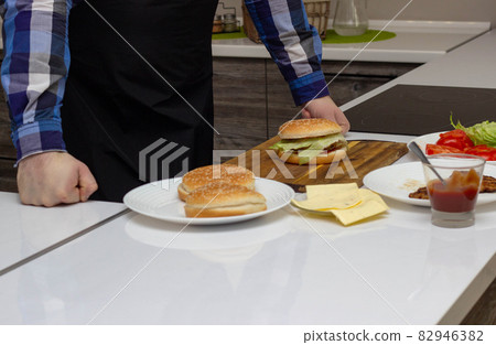 Man in black apron prepares homemade burgers with ingredients, copy space, cooking fast food Man in black apron prepares homemade burgers with ingredients, copy space, cooking fast food 82946382