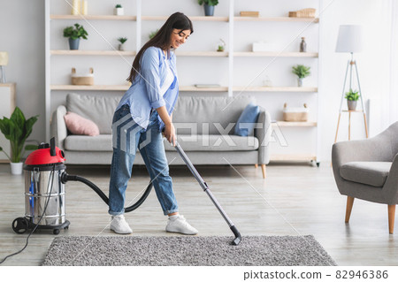 Cheerful woman cleaning rug carpet with vacuum cleaner Cheerful woman cleaning rug carpet with vacuum cleaner 82946386