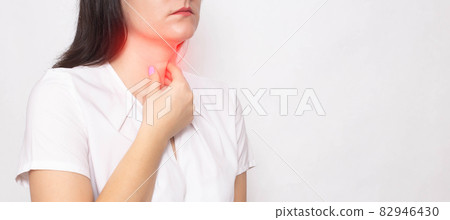 The girl holds on to the sore red throat on a white background. Concept of sore throat, laryngitis and sore throat in coronavirus. Copy space for text The girl holds on to the sore red throat on a white background. Concept of sore throat, laryngitis and sore throat in coronavirus. Copy space for text 82946430