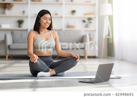 Online Yoga. Young asian woman using laptop for practicing meditation at home 82946691