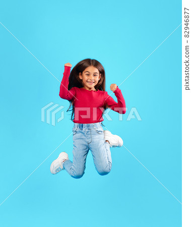 Little Girl Jumping Having Fun Posing In Mid-Air, Blue Background Little Girl Jumping Having Fun Posing In Mid-Air, Blue Background 82946877