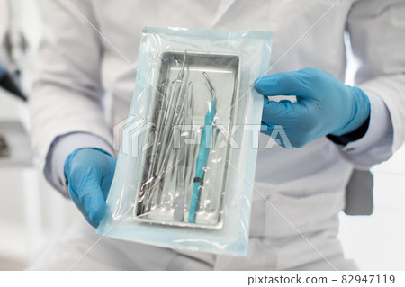 Doctor Wearing Blue Sterile Gloves Demonstating Sealed Sterilization Pouch With Dental Tools 82947119