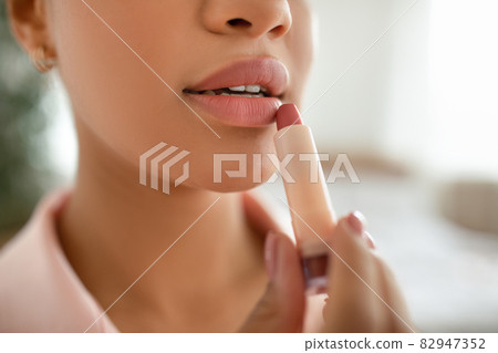 Young african american lady applying nude lipstick from tube, putting on decorative makeup, closeup, crop 82947352