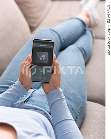 Woman Listening Music On Smartphone While Relaxing On Couch At Home 82947419