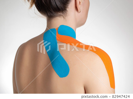 Fixation of muscles and ligaments on the girl's shoulder with blue and orange kinesiological tape, close-up. Taping in sports 82947424