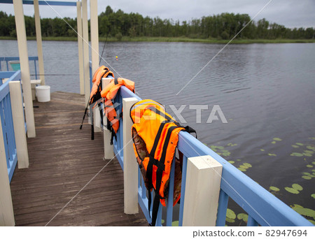 Orange life jackets and fishing equipment on the fishing bridge. The concept of safety behavior on the water, accident, drowning of a person. Copy space for text Orange life jackets and fishing equipment on the fishing bridge. The concept of safety behavior on the water, accident, drowning of a person. Copy space for text 82947694