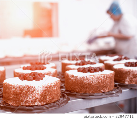 Pastry chef girl makes a cake from fresh biscuit berries and cream. Mass production of cakes and sweets, confectionery factory, professional 82947711
