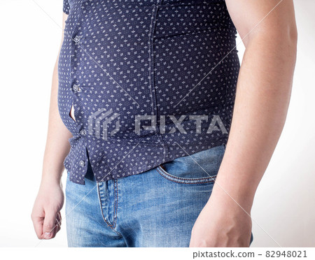 A man in a black tight shirt on a white background. Overweight, unhealthy diet and weight loss concept, close-up. Small clothing size A man in a black tight shirt on a white background. Overweight, unhealthy diet and weight loss concept, close-up. Small clothing size 82948021