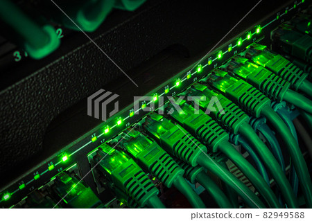 Close up of green network cables from data center connected with patch cord to black switch glowing in the dark 82949588