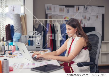 A lovely Asian woman fashion designer sits at her workstation in her studio, stares at the webcam, and speaks through video call. A lovely Asian woman fashion designer sits at her workstation in her studio, stares at the webcam, and speaks through video call. 82951988
