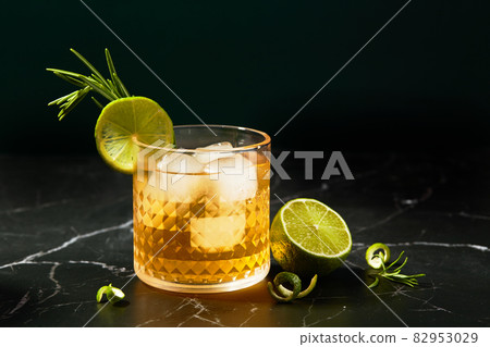 Alcoholic or non-alcoholic cocktail with lime and rosemary on a dark marble table 82953029
