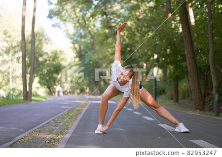 Woman runner stretching legs before exercising summer park morning Woman runner stretching legs before exercising summer park morning 82953247