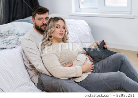 Happy family concept. Husband hug belly pregnant wife sitting floor indoor living room near sofa 82953281