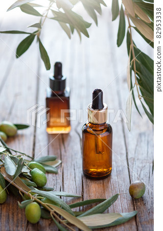 Olive based cosmetic amber bottles with serum or lotion on wooden background with sprig branches from olive tree. Olive based cosmetic amber bottles with serum or lotion on wooden background with sprig branches from olive tree. 82953338