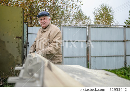 An elderly carpenter saws the board with a circular saw. 82953442