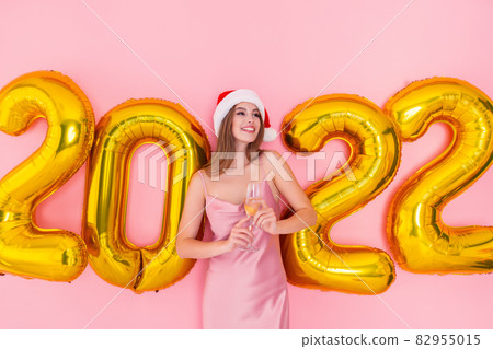 Smiling woman hold glass of champagne in Santa's hat look sideways.golden air balloons 2022 New Year 82955015