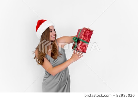happy young woman in Santa's hat raises up present while stands on white background. Celebration happy young woman in Santa's hat raises up present while stands on white background. Celebration 82955026