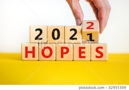 Business concept of planning 2022 hopes symbol. Businesman turns a wooden cube and changes words 'Hopes 2021' to 'Hopes 2022'. Beautiful white background, copy space. Business and hopes 2022 concept. Business concept of planning 2022 hopes symbol. Businesman turns a wooden cube and changes words 'Hopes 2021' to 'Hopes 2022'. Beautiful white background, copy space. Business and hopes 2022 concept. 82955309