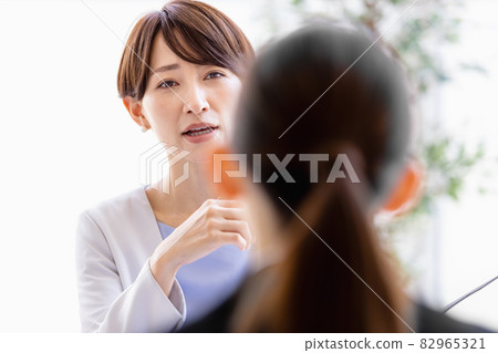 Middle-aged woman talking to a woman in a suit sitting face to face 82965321