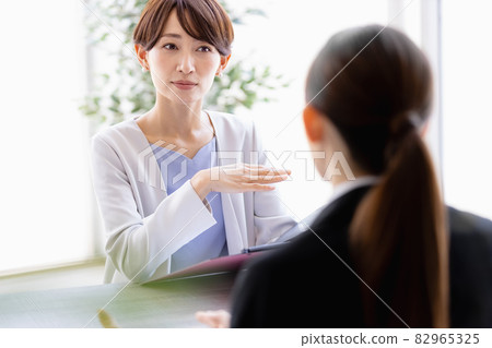 Middle-aged woman talking to a woman in a suit sitting face to face 82965325