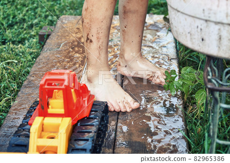 Boy in shorts with dirty legs playing with water in yard 82965386