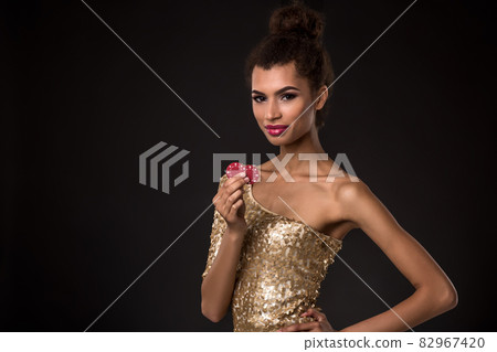 Woman winning - Young woman in a classy gold dress holding two red chips, a poker of aces card combination. 82967420