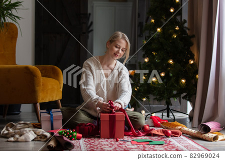 Woman wrapping Christmas gifts at home on a floor. Woman wrapping Christmas gifts at home on a floor. 82969024