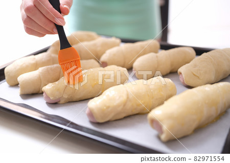 Female chef applies brush of egg yolk to croissants closeup Female chef applies brush of egg yolk to croissants closeup 82971554