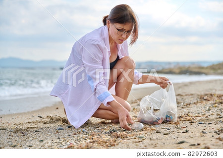 Mature woman tourist relaxing on the beach collecting plastic trash in a bag 82972603
