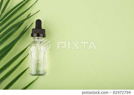 Skin serum in transparent bottle on light green background with palm leaf Skin serum in transparent bottle on light green background with palm leaf 82972794
