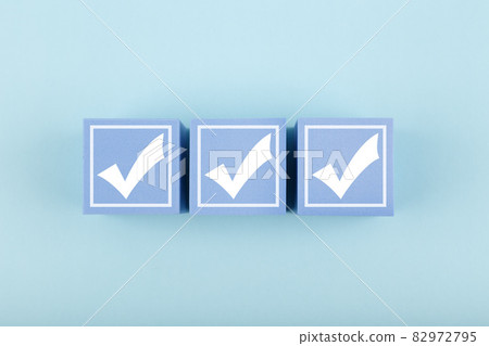 Three white checkmarks on blue cubes against bright pastel blue background Three white checkmarks on blue cubes against bright pastel blue background 82972795