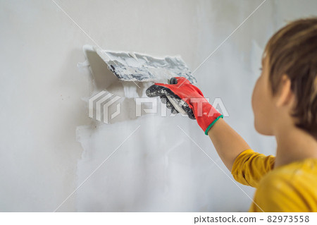 Boy makes repairs at home, he teaches children to plaster the walls with a spatula in his hands Boy makes repairs at home, he teaches children to plaster the walls with a spatula in his hands 82973558