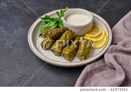 Traditional dish dolma or sarma, with parsley, saucepan with sour cream and lemon with napkin Traditional dish dolma or sarma, with parsley, saucepan with sour cream and lemon with napkin 82973561