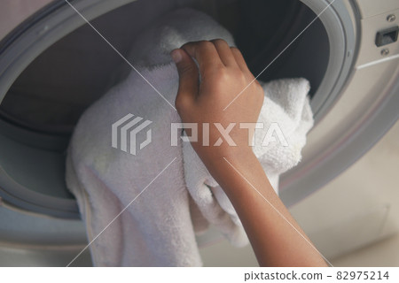 man putting shirt into washing machine. 82975214