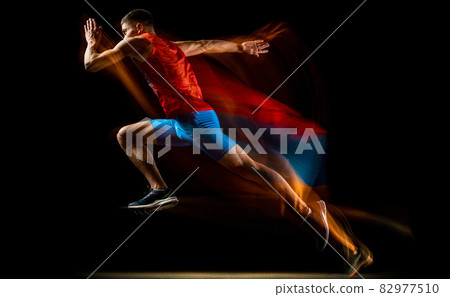 Cropped portrait of young athletic man, professional runner training isolated over black background. Stroboscope effect. In motion Cropped portrait of young athletic man, professional runner training isolated over black background. Stroboscope effect. In motion 82977510