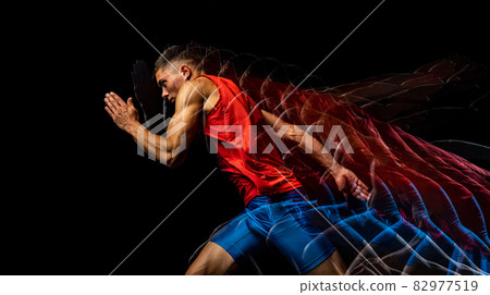 Cropped portrait of young athletic man, professional runner training isolated over black background. Stroboscope effect. 82977519
