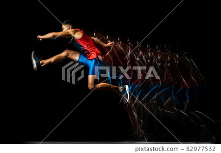 Full-length portrait of young man, professional track athlete, runner in a jump, training isolated over black background. Stroboscope effect. Full-length portrait of young man, professional track athlete, runner in a jump, training isolated over black background. Stroboscope effect. 82977532