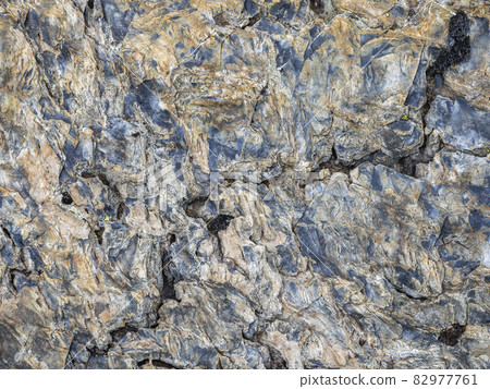 Wavy texture of the stone. Multicolored detailed texture of a rocky mountain slope. Geological rock. 82977761