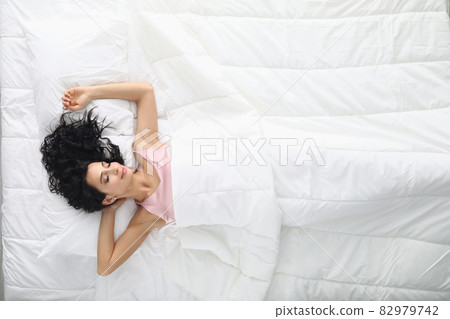Young woman with curly hair sleeping in white bed top view Young woman with curly hair sleeping in white bed top view 82979742