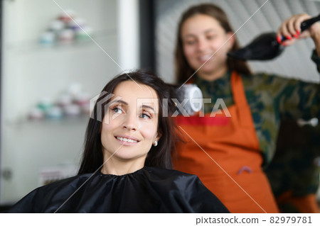 Woman hairdresser drying and straightening client hair with brushing and hairdryer 82979781