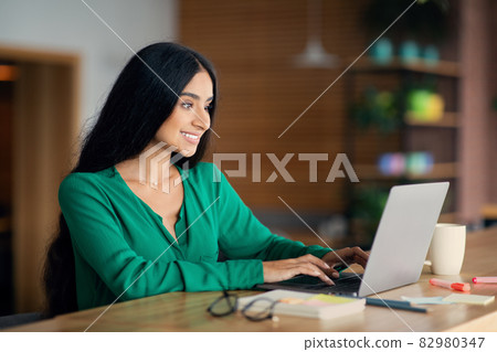 Happy indian woman freelancer enjoying her job, cafe interior Happy indian woman freelancer enjoying her job, cafe interior 82980347