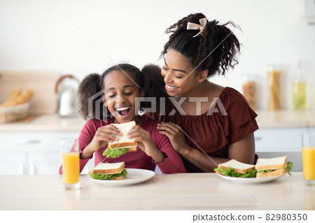 Loving black mother and daughter cuddling while having snack Loving black mother and daughter cuddling while having snack 82980350