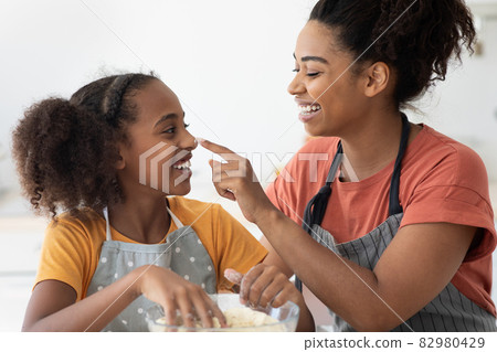 Closeup of black woman staining her daughter nose with flour 82980429