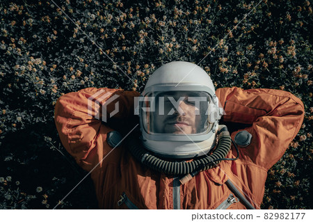 Closeup of cosmonaut wearing space suit and space helmet taking a nap while lying on grass outdoors. Portrait of astronaut sleeping on meadow Closeup of cosmonaut wearing space suit and space helmet taking a nap while lying on grass outdoors. Portrait of astronaut sleeping on meadow 82982177