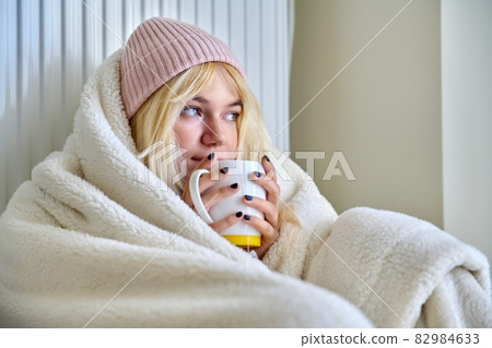 Young female teenager warming herself with blanket, heating radiator, hot tea 82984633