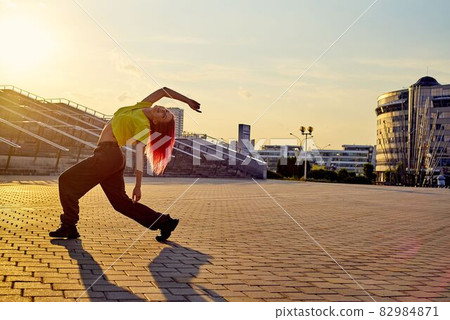athletic sporty woman with dyed pink hair dances street dance against background of sunset 82984871