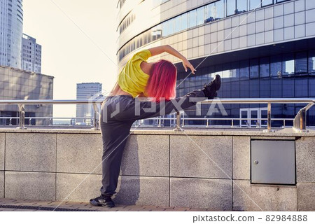 sporty woman in a yellow T-shirt and dyed pink hair stretches her legs before training sporty woman in a yellow T-shirt and dyed pink hair stretches her legs before training 82984888
