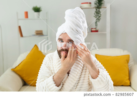 Bearded man sitting with eye patches on his face. Wrinkles and face home care for men. Bearded man sitting with eye patches on his face. Wrinkles and face home care for men. 82985607