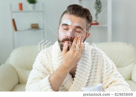 Bearded guy applying facial cream in front of mirror Skin care and spa for man concept. Bearded guy applying facial cream in front of mirror Skin care and spa for man concept. 82985609